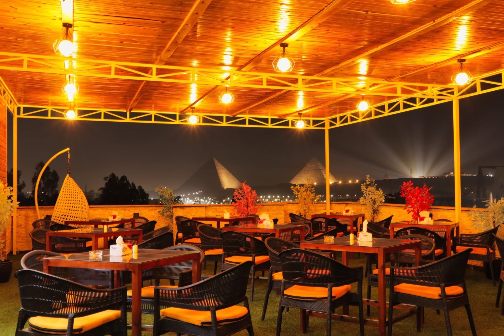 Grand View rooftop at night with warm lights and the illuminated Pyramids of Giza on the horizon